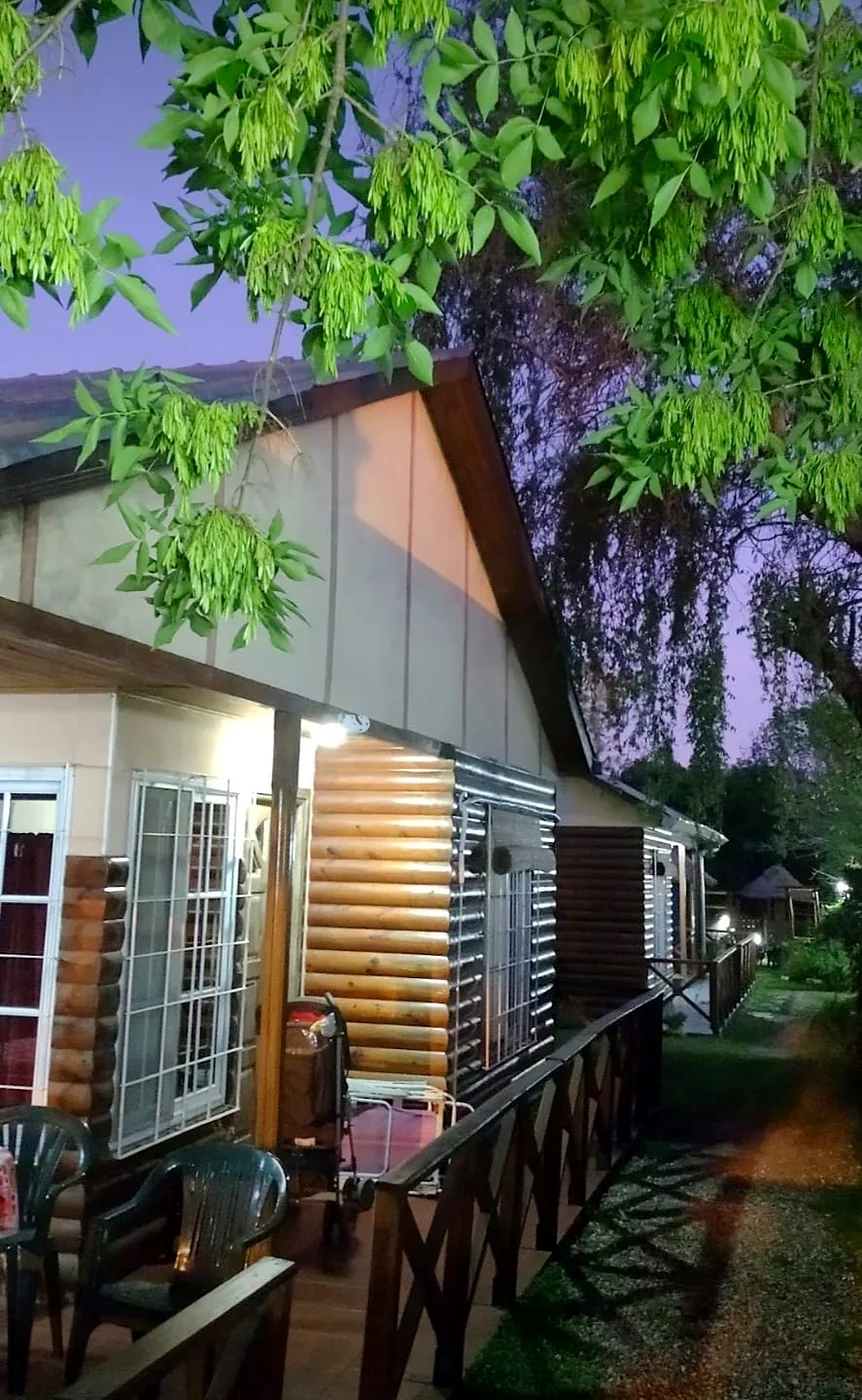 Cabañas de troncos iluminadas al anochecer, con galería y baranda de madera