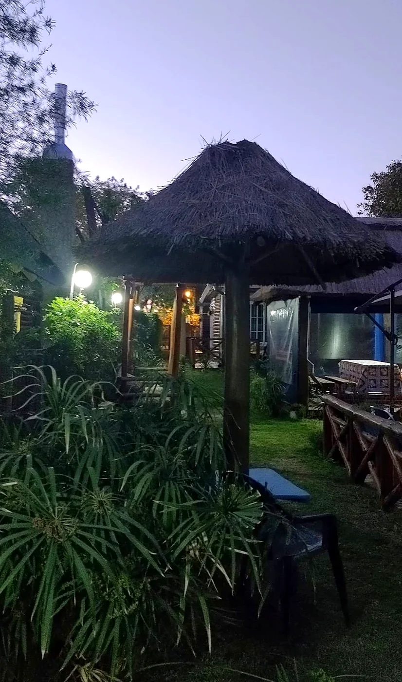 Parque al anochecer, con sombrilla de paja, farolas y plantas